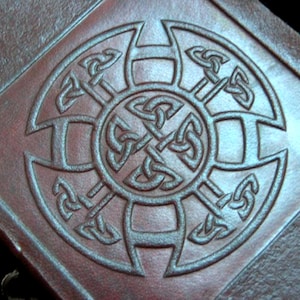 May include: A brown leather journal with a Celtic knot design embossed on the cover.