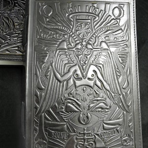 Peut inclure: Un journal reli&eacute; en cuir noir avec un motif en relief d'une figure ail&eacute;e et cornue avec un troisi&egrave;me &oelig;il. Les mots "Solve" et "Dracula" sont en relief au bas de la couverture.