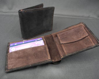 Puede incluir: Una cartera negra de dos pliegues hecha de material similar al ante, con un interior marrón y ranuras para tarjetas visibles. La cartera está abierta, mostrando el interior, y otra cartera cerrada está en el fondo.