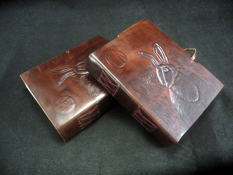 Pode incluir: Dois di&aacute;rios de couro castanho com um design de coelho e lua gravado &agrave; m&atilde;o. Os di&aacute;rios t&ecirc;m um detalhe de costura decorativo na lombada.