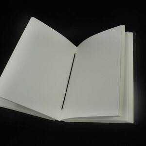 Peut inclure: Un carnet blanc vierge avec une reliure noire, ouvert &agrave; une nouvelle page. Le carnet est pos&eacute; &agrave; plat sur une surface noire.