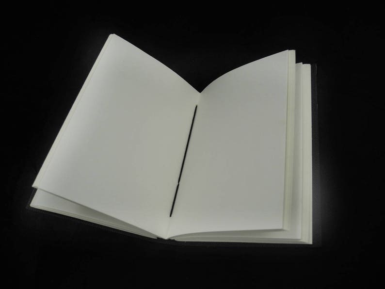 Peut inclure: Un carnet blanc vierge avec une reliure noire, ouvert &agrave; une nouvelle page. Le carnet est pos&eacute; &agrave; plat sur une surface noire.
