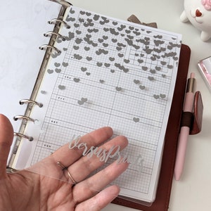 Planificador transparente con texto personalizado en vinilo plateado mate y corazones. Inserto para anillas de tamaño A5, A6, tamaño personal y de bolsillo.