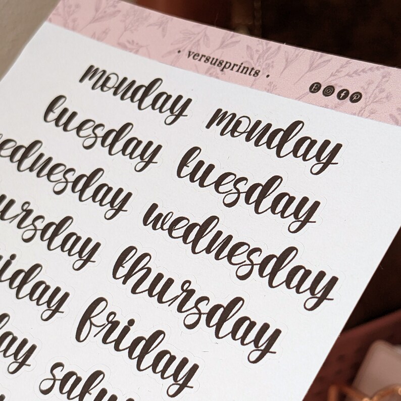 May include: A sheet of stickers with the days of the week written in cursive script. The stickers are black and white and are printed on a white background.