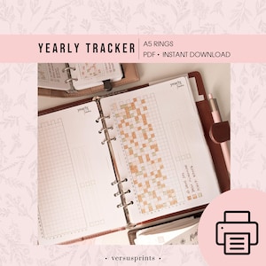 Può includere: Raccoglitore ad anelli A5 aperto con un layout di monitoraggio annuale. Le pagine sono di colore chiaro con un design a griglia e il testo "YEARLY TRACKER" e "A5 RINGS PDF • INSTANT DOWNLOAD". È visibile una penna rosa.
