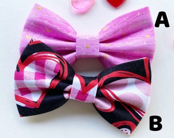 Könnte beinhalten: Zwei Stoff-Fliegen. Die obere Fliege ist pink mit einem weißen und goldenen Muster. Die untere Fliege ist schwarz mit einem weißen und roten Karomuster. Die Fliegen liegen auf einer weißen Oberfläche.