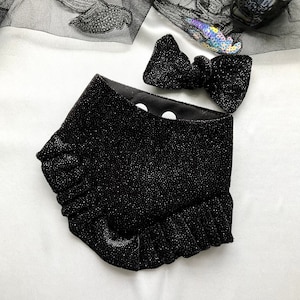 以下が含まれることがあります： 黒いキラキラ光るペット用バンダナと、お揃いの蝶ネクタイ。バンダナはフリルエッジで、内側には白い水玉模様があります。蝶ネクタイはシンプルなリボン型です。どちらもキラキラした生地で作られています。