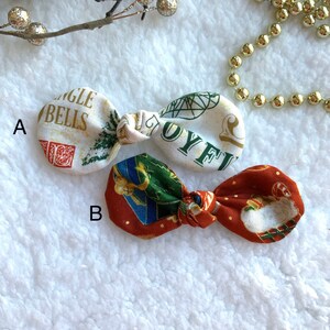 May include: Two Christmas-themed fabric hair bows. Bow A is white with red and green accents and the text "Jingle Bells". Bow B is red with green and blue accents.