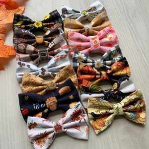 May include: Ten different bow ties with various fall-themed patterns, including autumn leaves, coffee cups, and Thanksgiving turkeys. The bow ties are made of fabric and have a variety of colors, including brown, orange, red, and green.