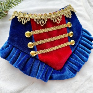 May include: A blue and red velvet dog collar with gold trim and rhinestones. The collar has a ruffled edge.