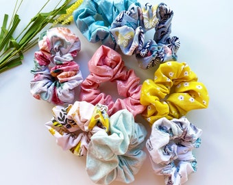May include: Assortment of colorful fabric scrunchies with floral and geometric patterns. The scrunchies are made of soft, stretchy fabric and are perfect for holding hair in place.