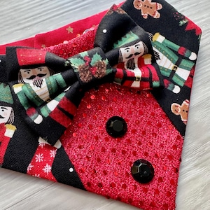 May include: A festive headband featuring a red sequined section with two black gem accents. The headband has a black and red patterned bow with nutcracker and gingerbread man designs, perfect for holiday celebrations.