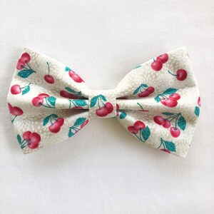 May include: A white bow tie with a cherry print. The cherries are red with green stems and leaves.