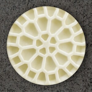 May include: A white circular soap dish with a geometric design. The design is made up of many small, raised squares and rectangles.