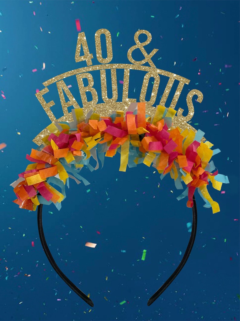 May include: A black headband with a gold glitter crown that says "40 & FABULOUS" on it. The crown is decorated with colorful tissue paper streamers.