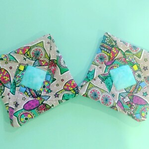 May include: Two square fabric pouches with a colorful, abstract pattern. Each pouch has a light blue square in the center.