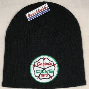 May include: Black knitted beanie hat with an embroidered circular patch. The patch features the words "Casino CLUB 1973" in white and red, with a green border. The tag reads "Beechfield ORIGINAL HEADWEAR".