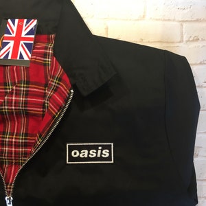 May include: Black jacket with a red and yellow tartan lining and a white "oasis" patch on the front.