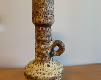 May include: A yellow and brown ceramic vase with a textured surface and a small handle. The vase has a bulbous base and a tall, slender neck.