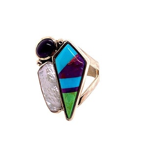 May include: A silver ring with a turquoise, purple, and green stone inlay in a diamond shape. The ring also features a black stone and a white pearl.