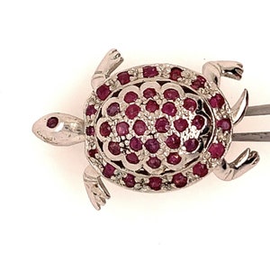 Puede incluir: Un broche de plata en forma de tortuga con un diseño detallado. El caparazón de la tortuga está cubierto de pequeñas piedras preciosas rojas.