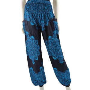 May include: Black harem pants featuring a vibrant blue floral mandala pattern. These pants have a wide, smocked elastic waistband and elasticized cuffs at the ankles. The design includes side pockets and a loose, relaxed fit throughout the legs.