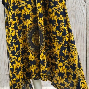 May include: A navy blue dress featuring a vibrant gold-colored ornate scrollwork pattern throughout. The fabric displays a prominent circular medallion design in the center, complemented by a decorative border along the hemline with intricate details.