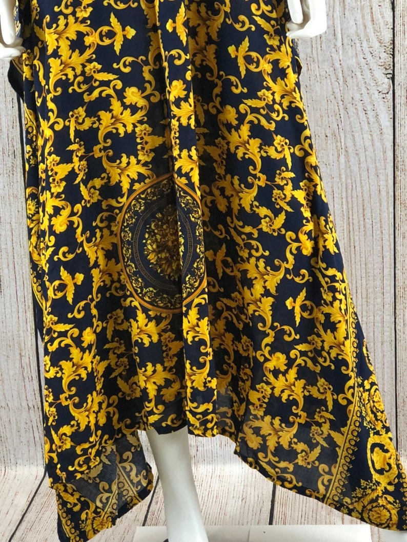 May include: A navy blue dress featuring a vibrant gold-colored ornate scrollwork pattern throughout. The fabric displays a prominent circular medallion design in the center, complemented by a decorative border along the hemline with intricate details.