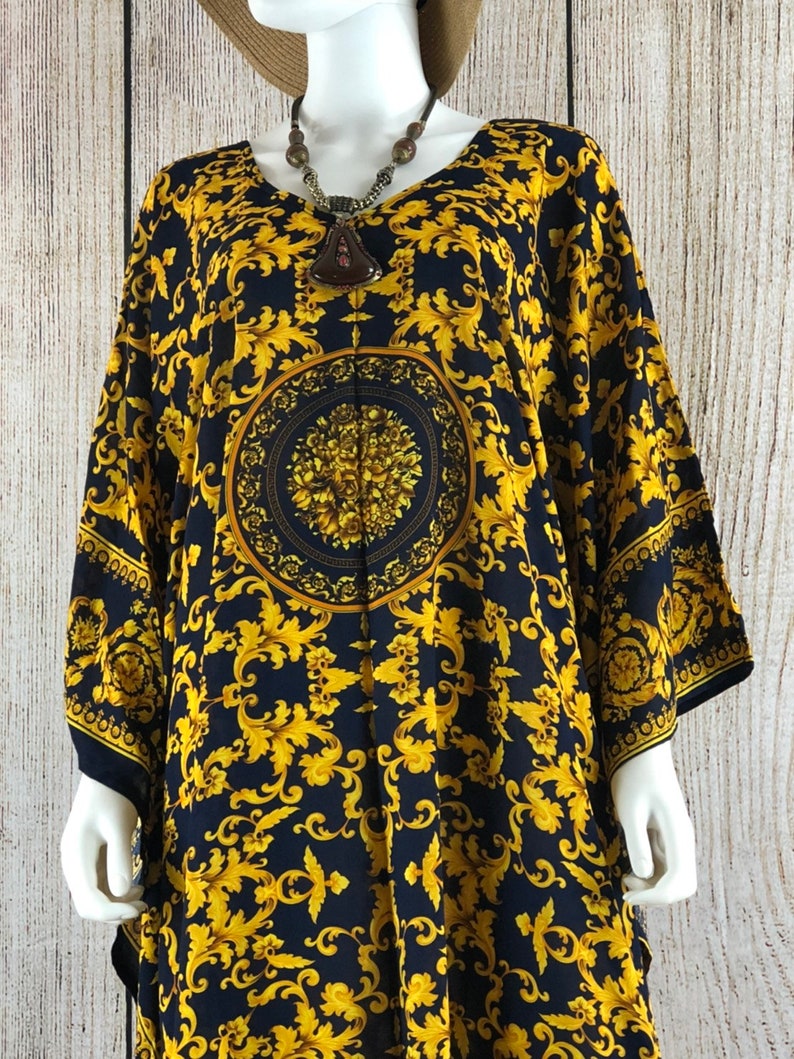 May include: A loose-fitting kaftan dress featuring a dark navy blue base with a vibrant gold-colored ornate acanthus leaf pattern. The garment includes a central circular medallion design with floral details and wide, flowing sleeves.