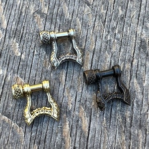 Könnte beinhalten: Drei Metallschließen mit einem strukturierten, schuppigen Design. Die Schließen sind silber, gold und schwarz.