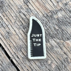 以下が含まれることがあります： 白と黒のパッチで、白い文字で「JUST THE TIP」と書かれています。