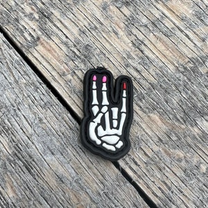 May include: A black and white skeleton hand patch with pink and red nail polish on the fingers. The patch is made of a soft, durable material and is perfect for adding a touch of personality to your clothing or gear.