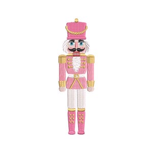 Könnte beinhalten: Ein gestickter Nussknacker in Rosa und Gold mit hohem Hut, Schnurrbart und weißem Bart. Der Soldat trägt eine rosa Uniform mit goldenen Akzenten und rosa Stiefeln. Eine festliche Weihnachtsdekoration.