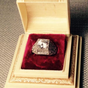 May include: A vintage ring box with a red velvet interior and a sparkling diamond ring with a silver band.