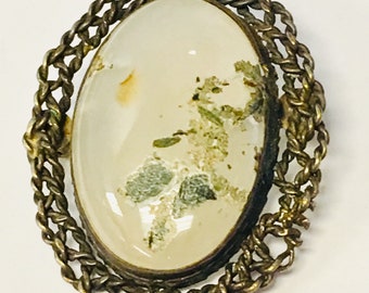 May include: A vintage oval-shaped brooch with a white agate stone set in a gold-toned chain link frame.
