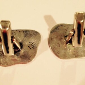 May include: A pair of silver cufflinks with a textured, irregular shape. Each cufflink has a circular stamp with the text "925" inside.
