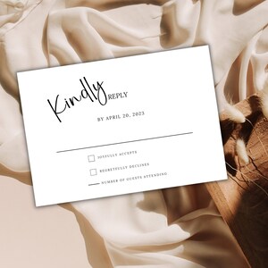 Può includere: Un biglietto RSVP bianco con testo nero. Il testo recita "Kindly Reply by April 20, 2023". Ci sono due caselle di controllo con il testo "Joyfully Accepts" e "Regretfully Declines". C'è una riga per il numero di ospiti che parteciperanno.
