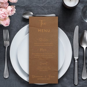 May include: A brown paper menu with gold lettering for a wedding reception. The menu lists the starters, main course, and dessert. The bottom of the menu reads "Shannen & Trever September 9, 2023".