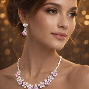 May include: A sparkling necklace and matching earrings set. The jewelry features a floral design with large pink gemstones surrounded by smaller clear stones. The necklace is worn on a person's neck, and the earrings dangle from the ear.