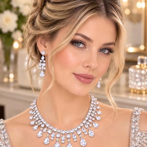 Könnte beinhalten: Ein silberfarbenes Set aus Halskette und Ohrhängern mit zahlreichen klaren, facettierten, runden und tropfenförmigen Steinen. Die Halskette hat ein mehrschichtiges Design mit herabhängenden tropfenförmigen Kristallen und die Ohrringe sind gestuft.