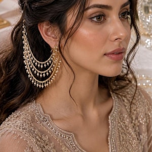 May include: A gold-toned ear cuff featuring three cascading chains adorned with small white pearls. The jewellery piece attaches to the ear and drapes along the side, creating a layered effect with delicate metal links and spherical pearl accents.