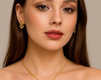 May include: A woman wearing a gold necklace and matching earrings. The jewelry features green and black gemstones. The necklace has a pendant with an ornate design. The earrings are small clusters of gemstones. The woman is wearing a black off-the-shoulder top.
