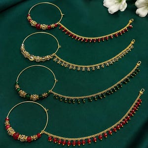 Pode incluir: Quatro argolas de nariz douradas com correntes anexadas, cada uma com um aro circular adornado com contas metálicas e cristais coloridos em vermelho, transparente e verde. Cada corrente é decorada com pequenas contas de cristal a condizer.