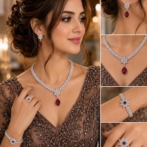 May include: A jewellery set consisting of a necklace, earrings, a bracelet, and a ring. Each piece features a silver-toned metal base with clear, sparkling stones arranged in a floral pattern, accented by a deep red, pear-shaped centre stone.