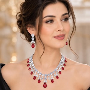 Peut inclure: Une parure de bijoux composée d'un collier et de boucles d'oreilles pendantes. Le collier présente une série de pierres claires rondes et taille marquise disposées en collier, agrémentées de pierres rouges en forme de poire suspendues.