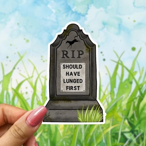 May include: A sticker featuring a tombstone design with the text "RIP SHOULD HAVE LUNGED FIRST." The tombstone has a silhouette of a dog jumping over a fence. The background is a watercolor scene of grass and sky.