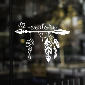 May include: White decal featuring an arrow with the word "explore" in a cursive font. The arrow is decorated with a heart, feathers, and dangling beads. A decorative swirl hangs below the arrow.