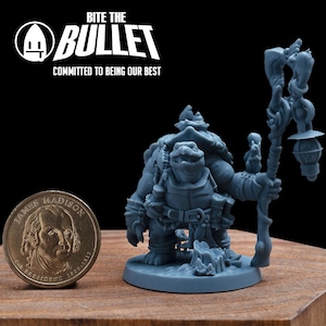May include: A blue-grey miniature figurine of a turtle-like character holding a staff with a lantern. A one-dollar coin is next to the figurine. The text "BITE THE BULLET" and "COMMITTED TO BEING OUR BEST" is in the upper left corner.