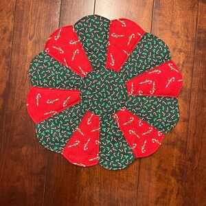 Puede incluir: Una falda redonda para árbol de Navidad con borde festoneado. La falda está hecha de tela roja y verde. Las secciones rojas tienen un patrón de bastón de caramelo, mientras que las secciones verdes tienen un patrón de bastón de caramelo blanco.