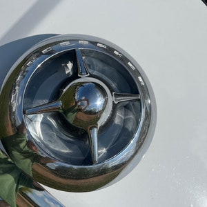 Könnte beinhalten: Ein verchromtes Autoemblem mit einem vierzackigen Sternmuster und dem Wort "DeSoto" am Rand.
